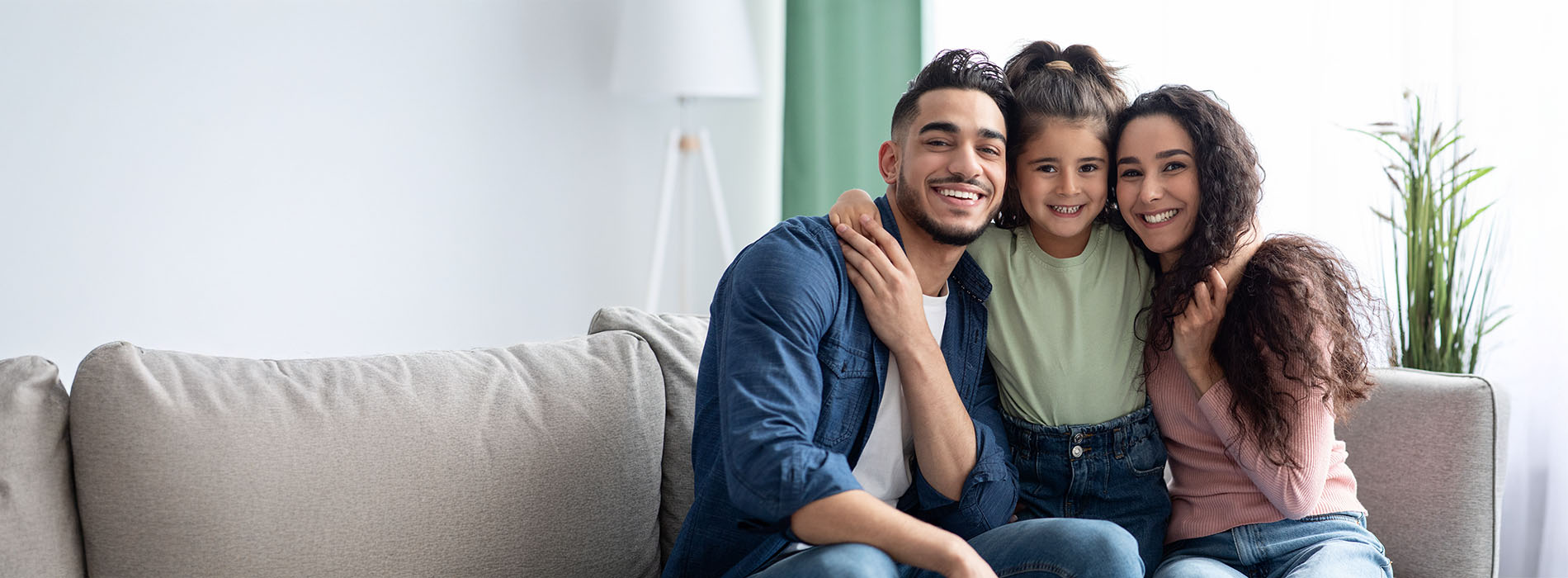 Three people sitting on a couch, smiling and looking at the camera.