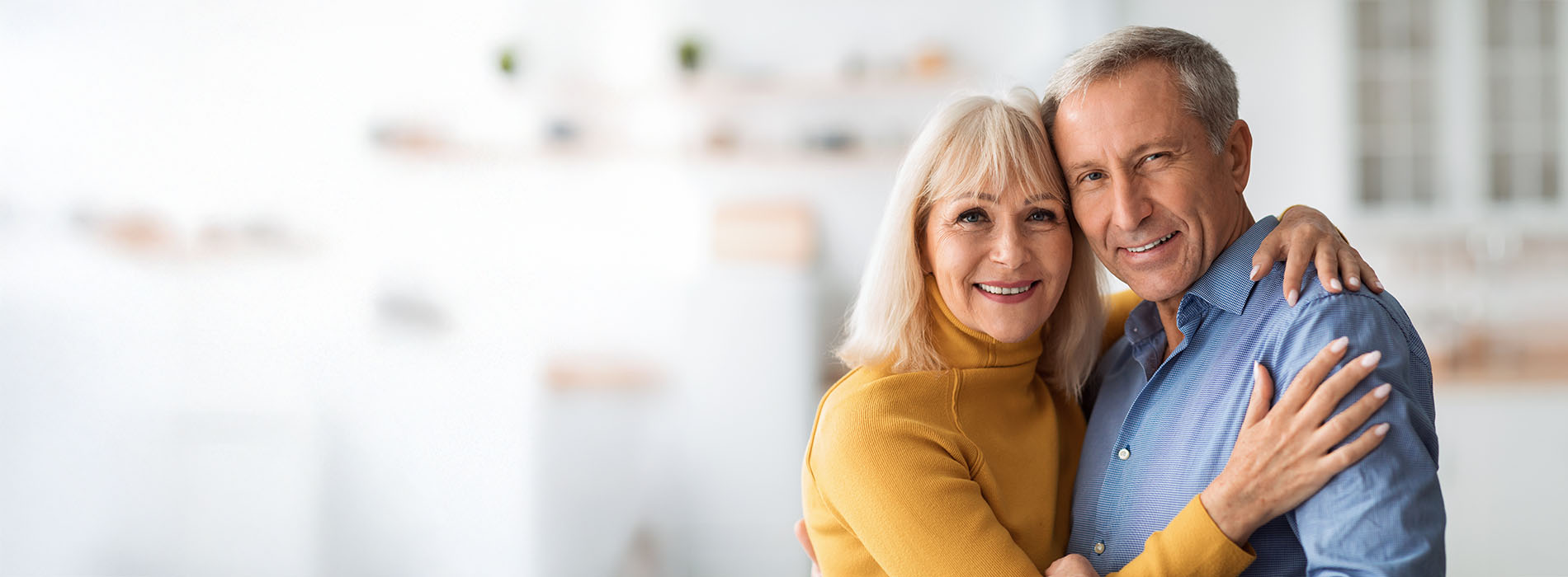 The image depicts an elderly couple embracing each other with smiles on their faces.