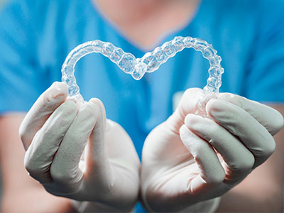 The image shows a person wearing gloves holding a clear plastic heart with a dental impression inside it.