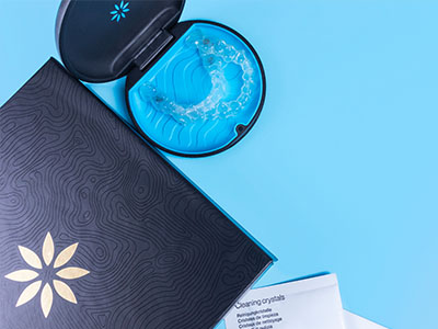 The image displays a blue toothbrush with bristles inside an open case next to a black box with a white star on top, suggesting dental care products are being advertised or displayed.