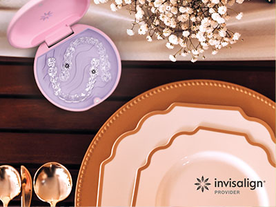 The image displays a collection of tableware items including plates, bowls, and a cake stand, all arranged on a wooden surface with decorative elements and a pink object that appears to be an eye makeup applicator.