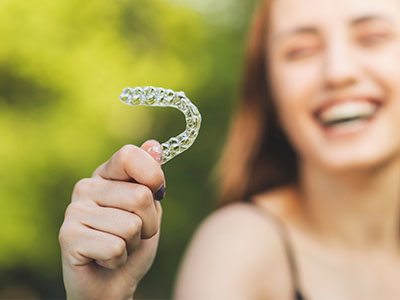 A smiling woman holds up a transparent dental impression tray with her right hand.