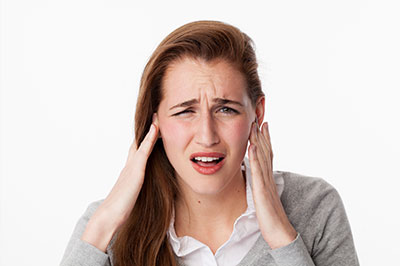 The image shows a woman with her hand on her head, appearing to be experiencing discomfort or pain, possibly related to hearing issues.