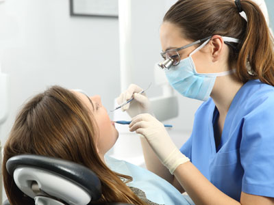 A dental hygienist performing a cleaning procedure on a woman s teeth while she receives treatment at a dental clinic.