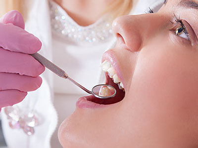 A woman receiving dental care with a dentist performing an examination using a mirror and dental instruments.