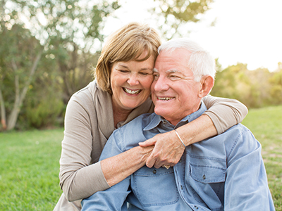 The image shows an elderly couple embracing each other outdoors during daylight hours.