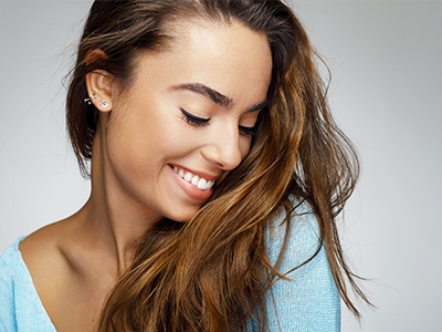 The image features a smiling woman with long hair, wearing a light blue top, against a plain background.