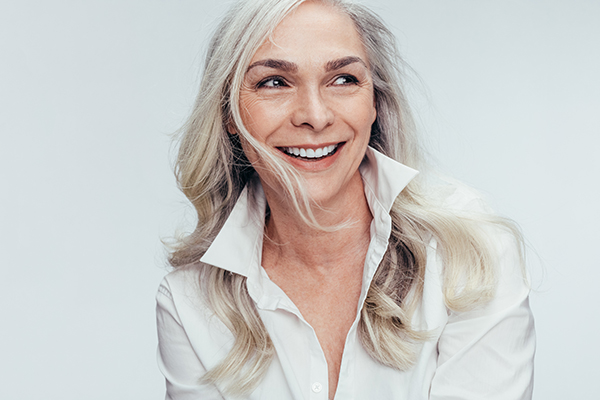 The image shows a woman with short hair smiling at the camera  she has a friendly expression and appears to be wearing a white top.