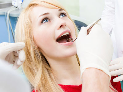 A woman sitting in a dental chair with her mouth open, receiving dental care from a professional wearing gloves and a mask.