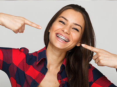 A woman with straight teeth pointing at her mouth with both hands.