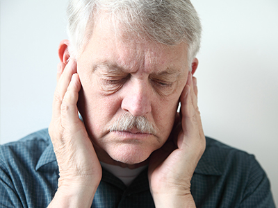 The image shows a man with his eyes closed, holding his face with both hands, appearing to be in pain or discomfort.